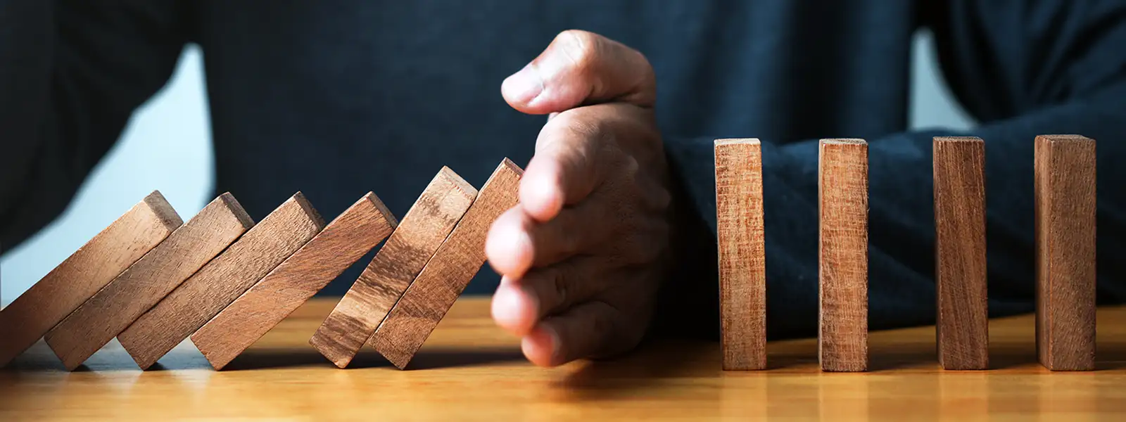 Hand Stopping Falling Dominoes